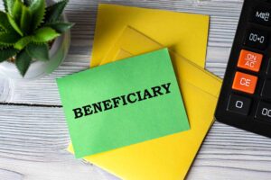 Green card labeled Beneficiary on desk with yellow folders, calculator, and plant, representing estate planning and inheritance.