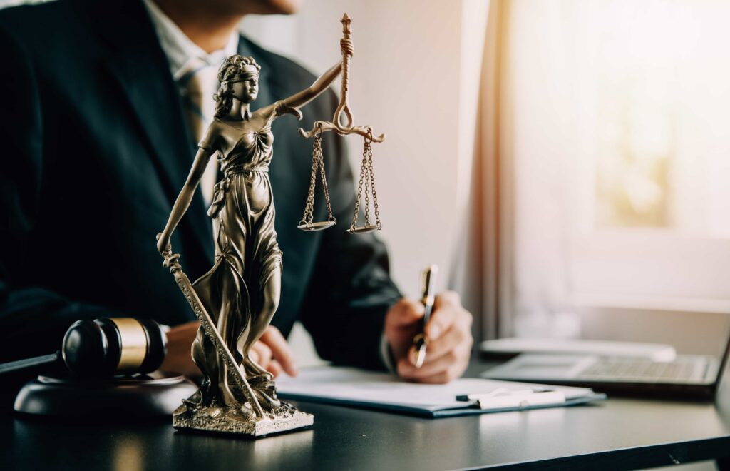 Lady Justice statue on a lawyer’s desk with gavel, documents, and laptop in a law office. Lady Justice statue on a lawyer’s desk with gavel, documents, and laptop in a law office.