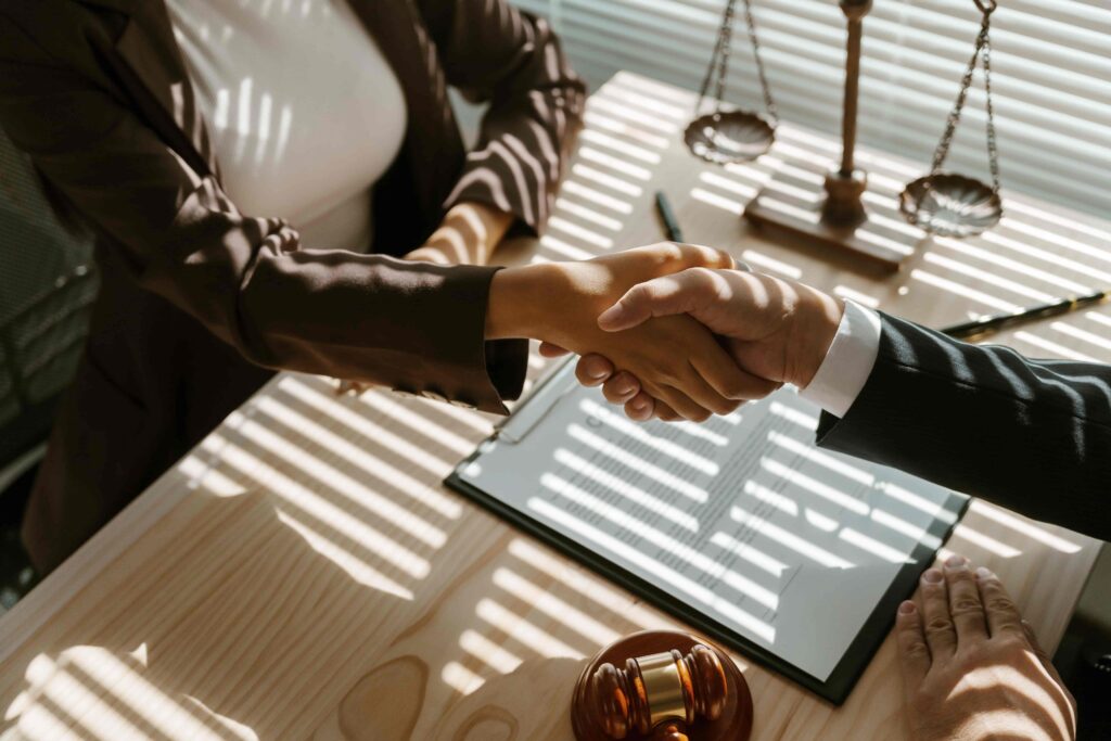 Lawyer and client shaking hands after signing legal agreement in law office with gavel and scales of justice on desk. Lawyer and client shaking hands after signing legal agreement in law office with gavel and scales of justice on desk.